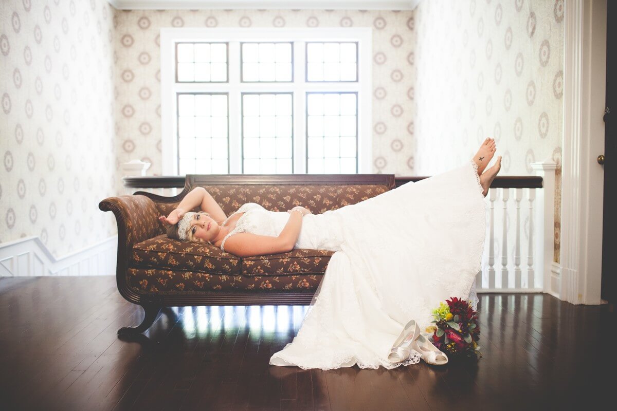 southern bride barefoot and reclining on vintage couch with shoes and bouquet displayed