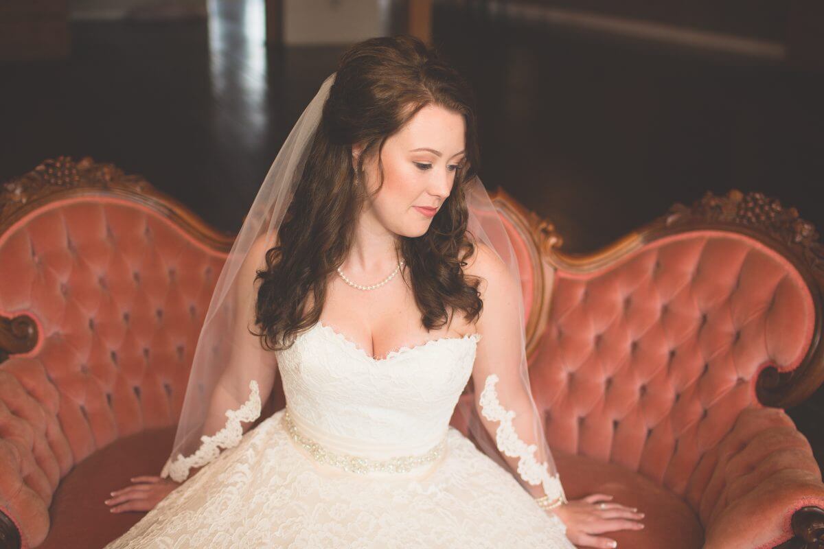 bride in white dress and veil sitting on vintage couch and looking down