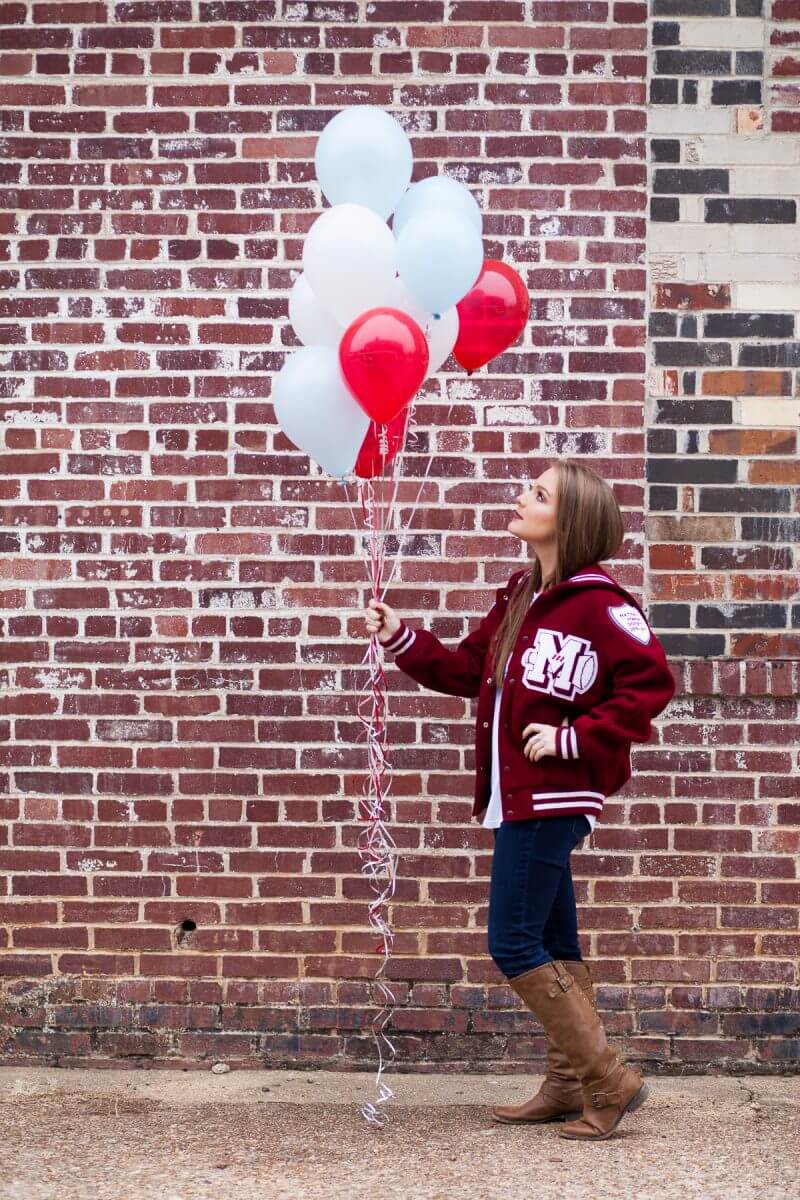 pretty high school senior in letter jacket and boots holding school color balloons