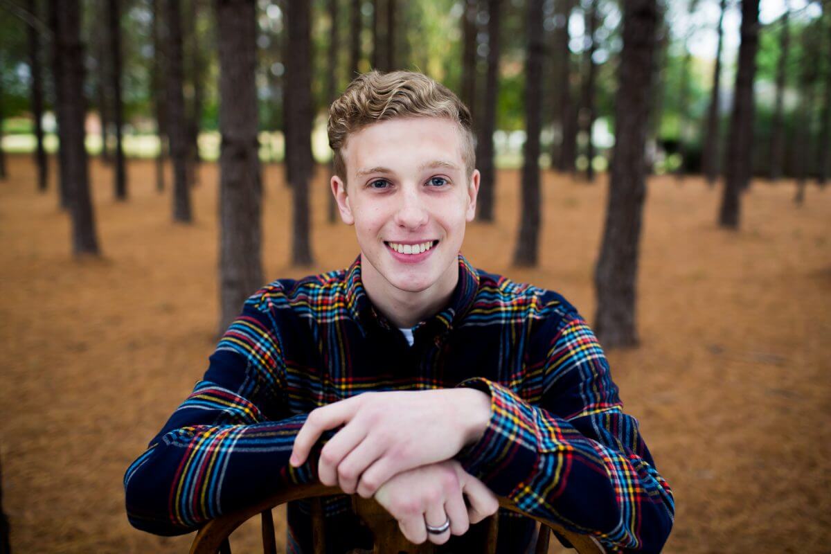 high school senior boy in bright plaid shirt in wooded park