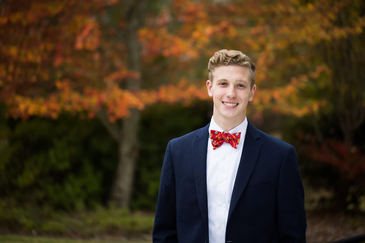 high school senior in sport coat and bow tie in front of fall trees