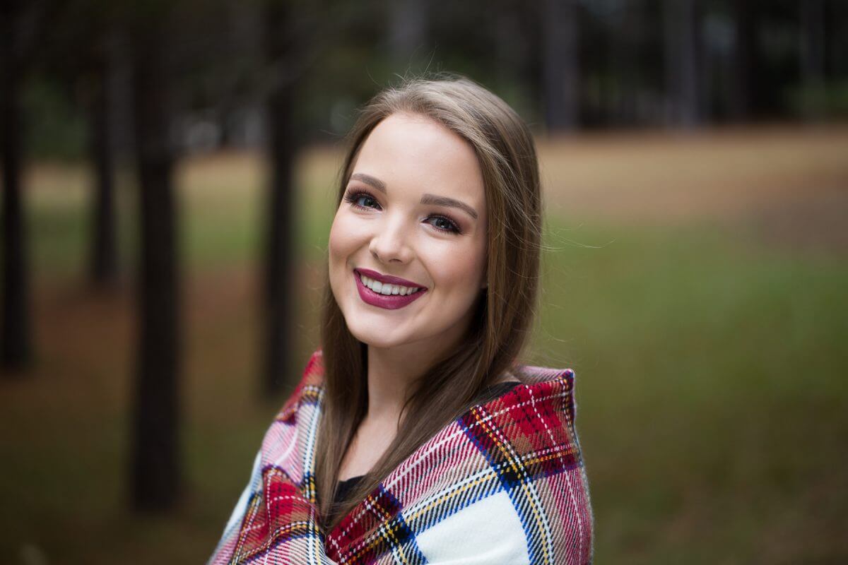 brunette in senior portrait headshot wearing red plaind blanket on shoulders