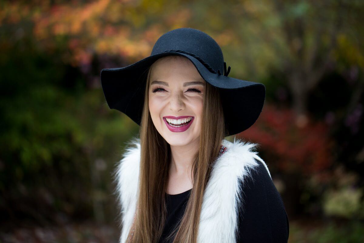 beautiful brunette in black floppy hat laughing in fall foliage
