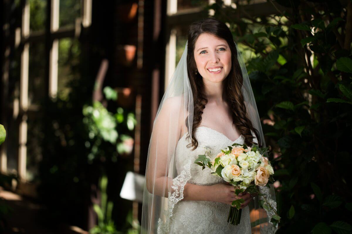 bride in white dress and veil holding pastel bouquet in conservatory