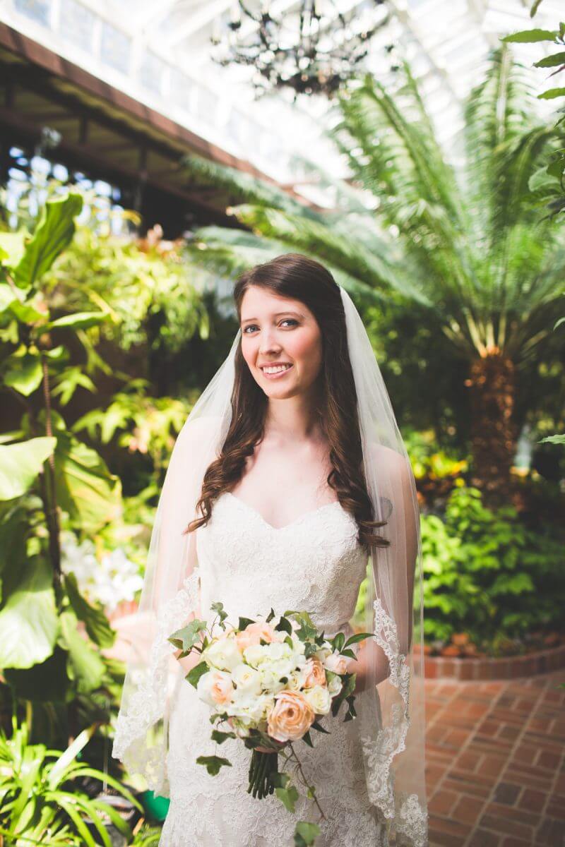 Smiling bride with bouquet and veil in conservatory