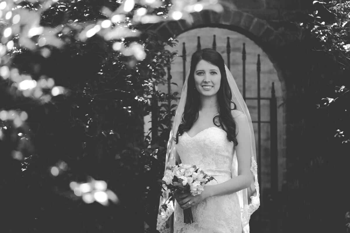 Bride with bouquet posing in front of wrought iron garden gate