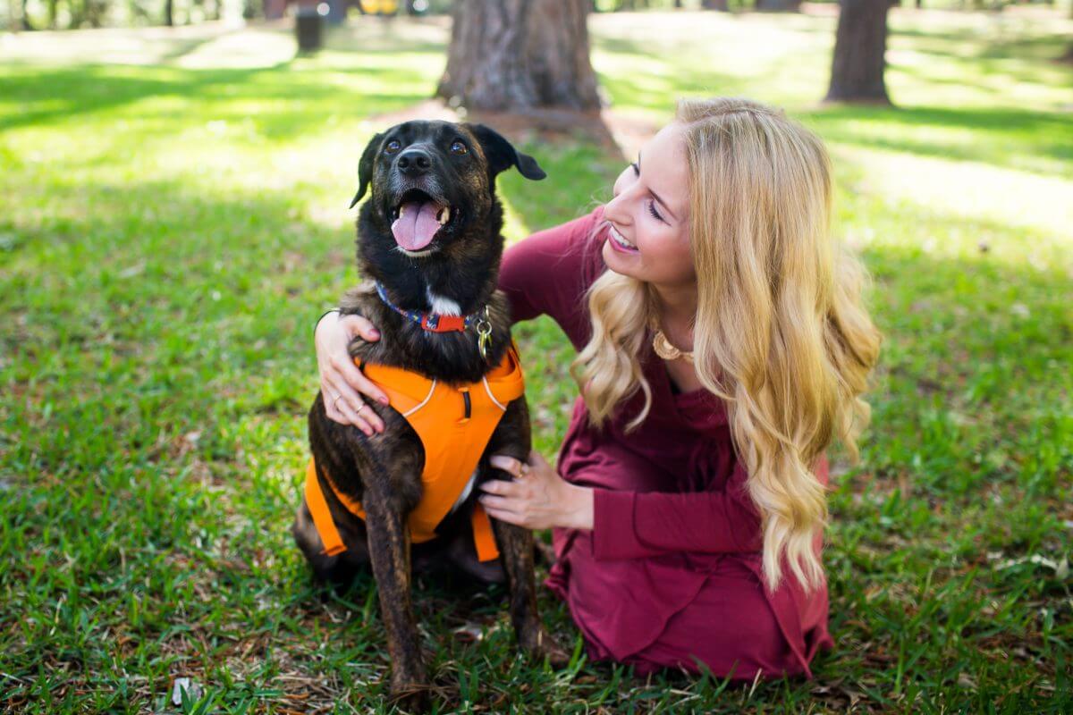 Blonde woman in red dress kneeling on ground and petting smiling dog
