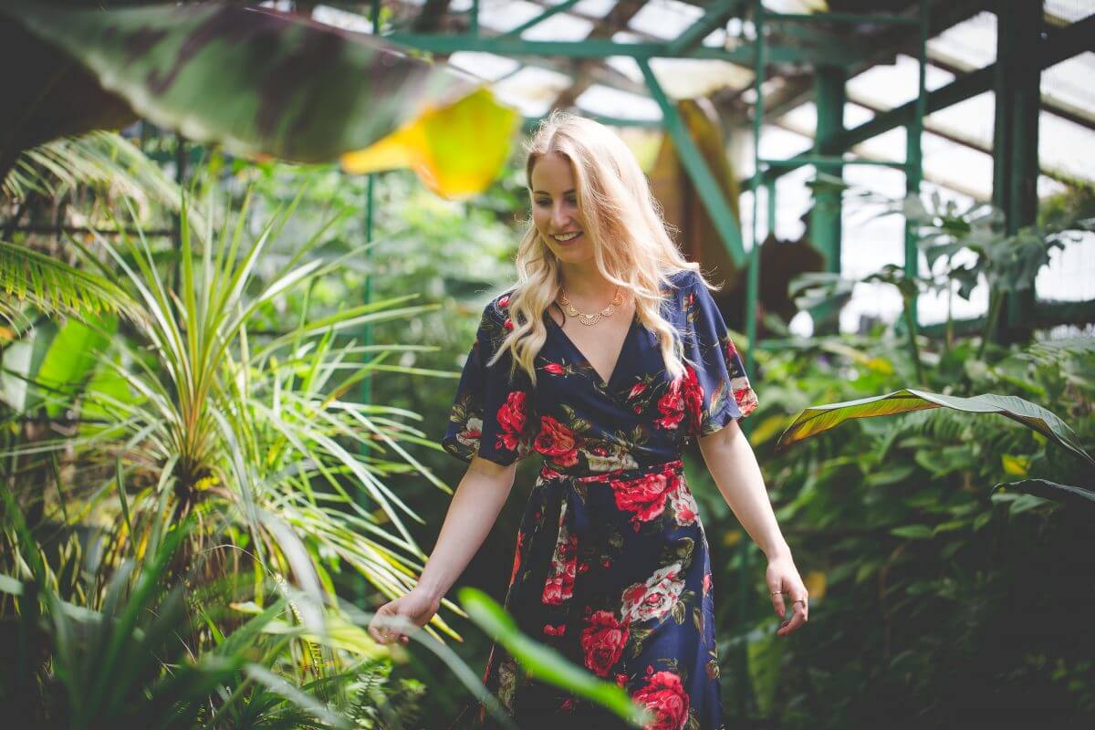 Blonde woman in blue floral dress walking among foliage in greenhouse
