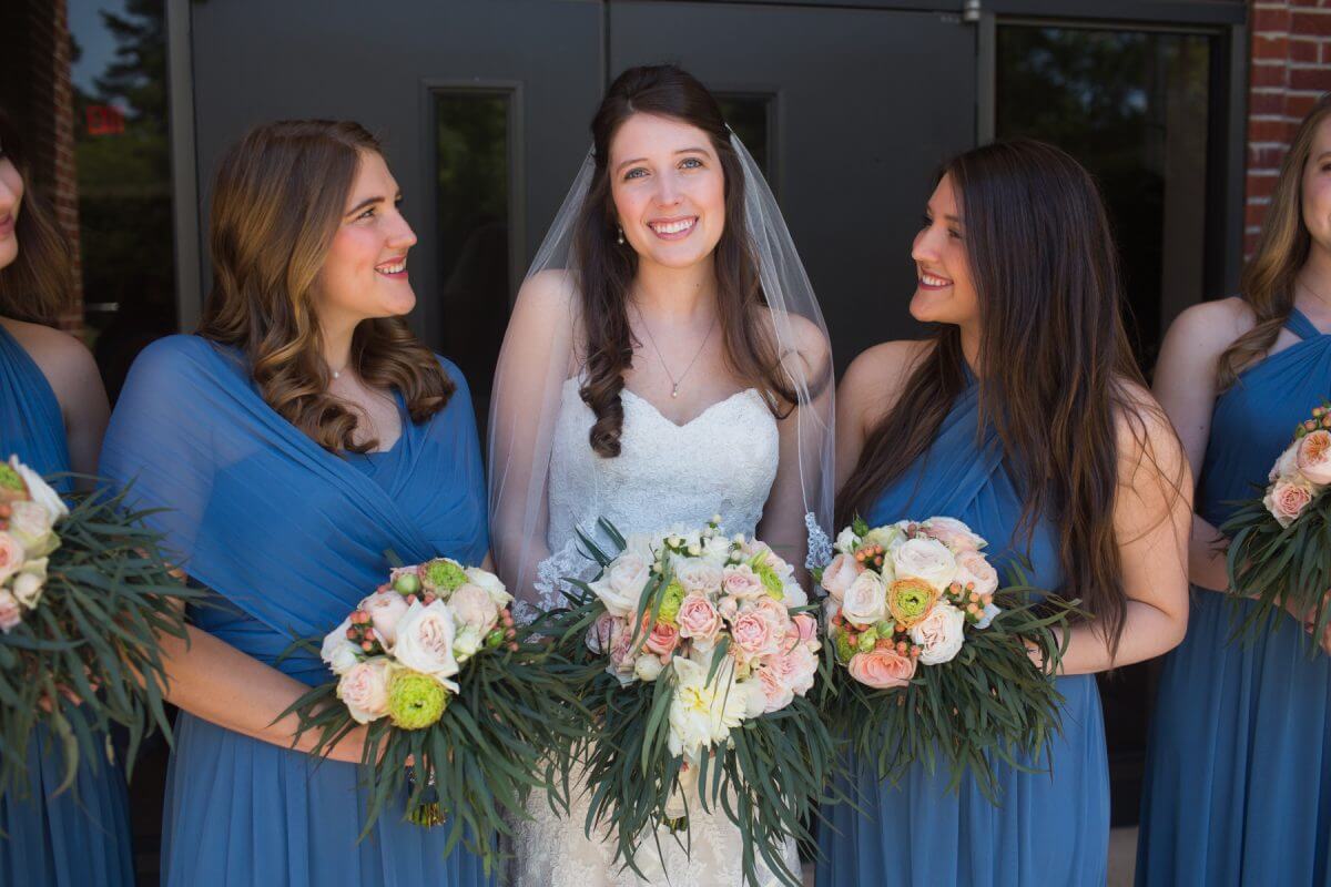 bridesmaids in blue dresses looking at smiling bride with bouquet