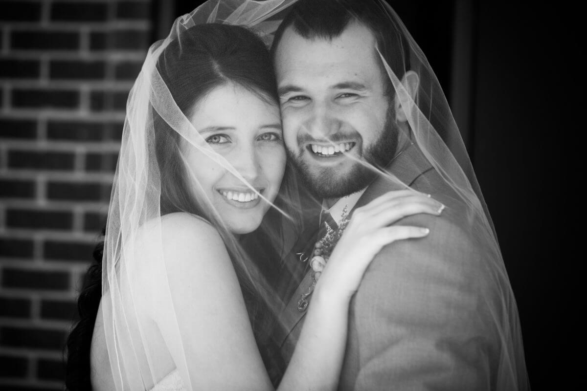 smiling bride and groom covered in bride's veil in black and white