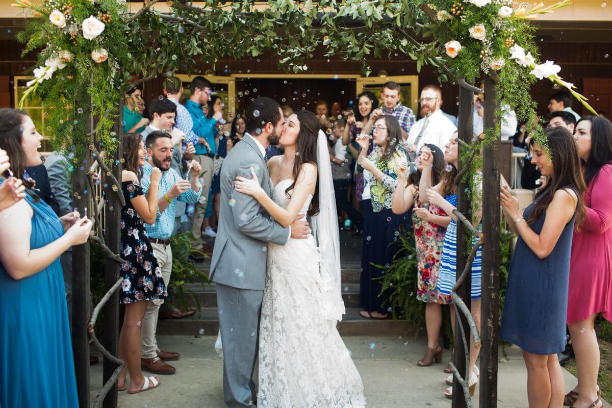bride and groom exit wedding reception and kiss under flowered pergola