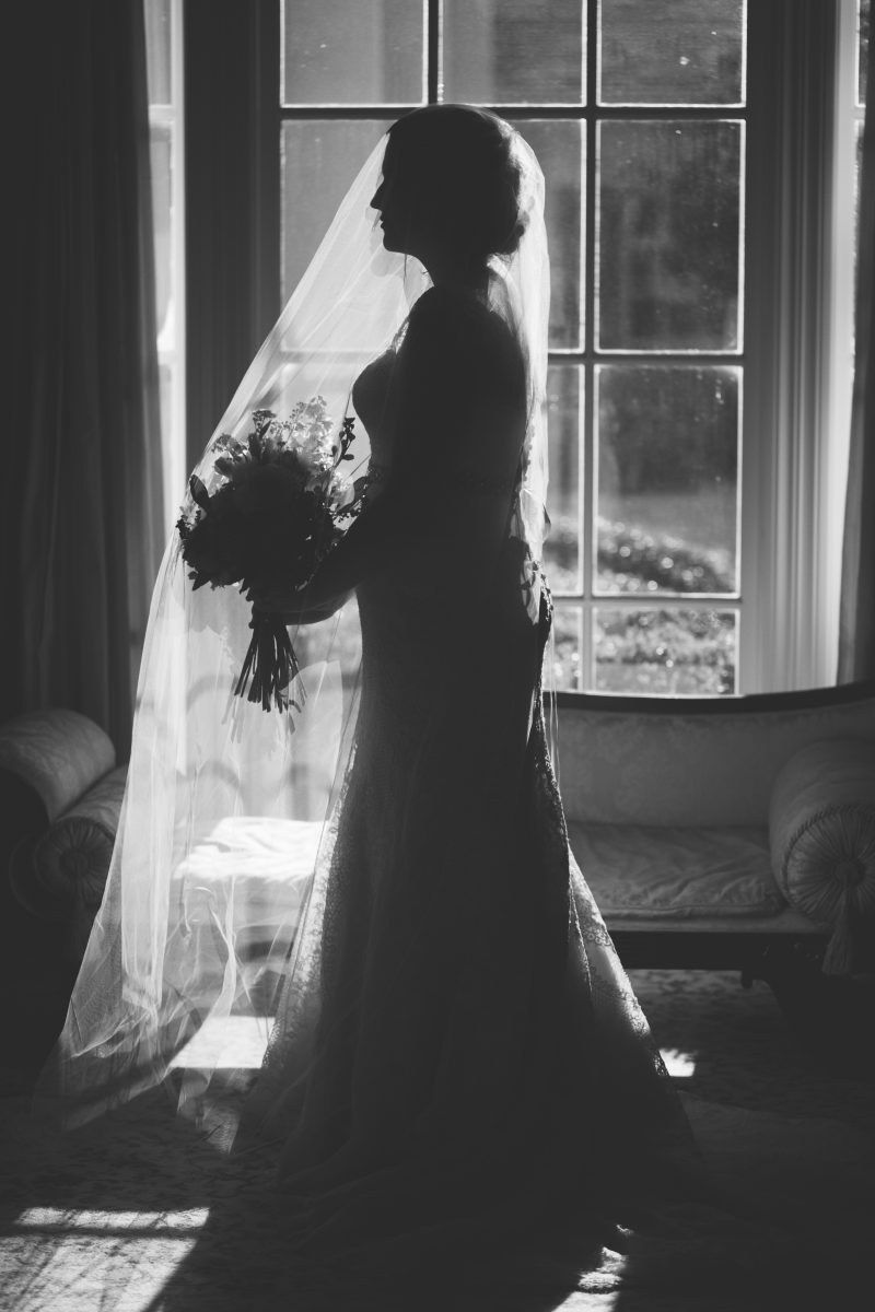 black and white silhouette of bride in profile with veil holding bouquet