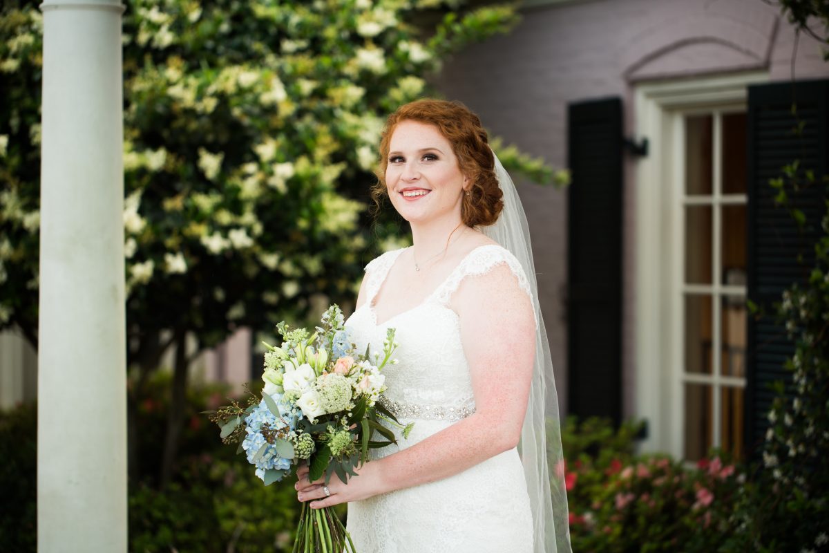 red headed bride smiling and holding bouquet near white column