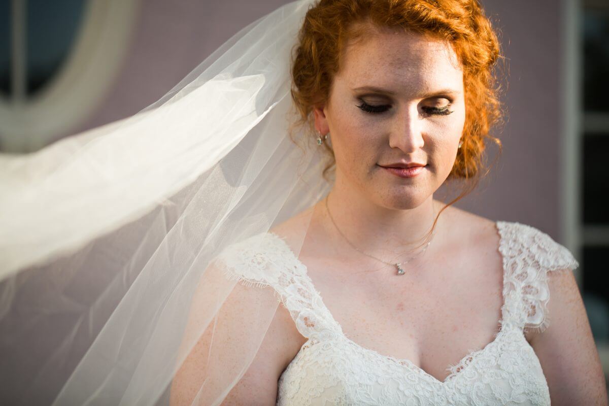 red headed bride standing in sunlight with long veil