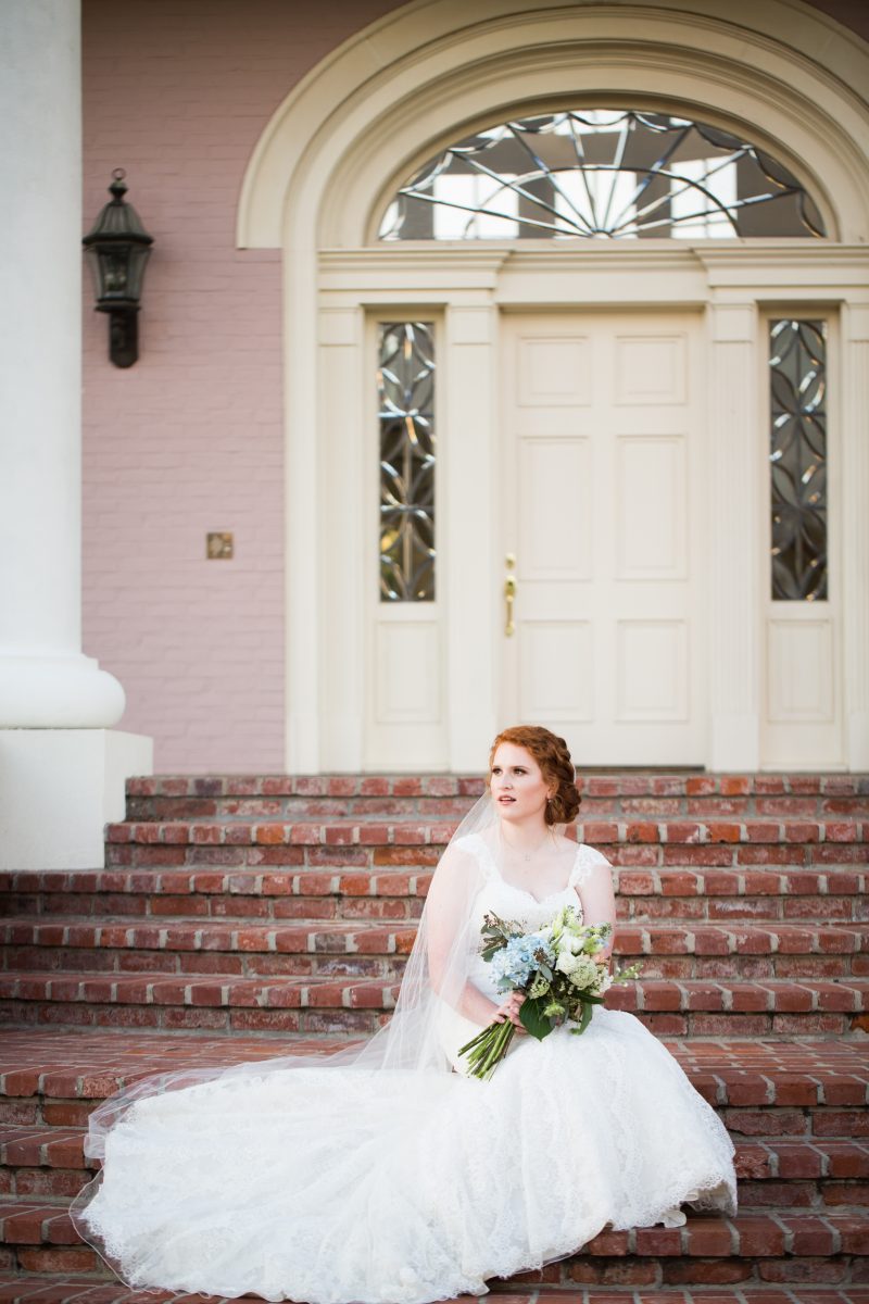 beautiful bride sitting on brick mansion steps with bouquet