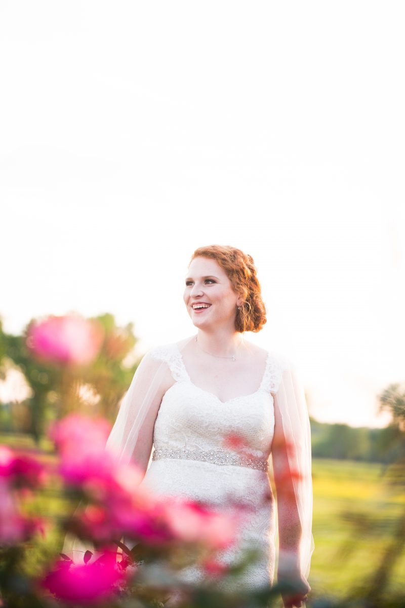 smiling red headed bride with pink flowers in foreground 