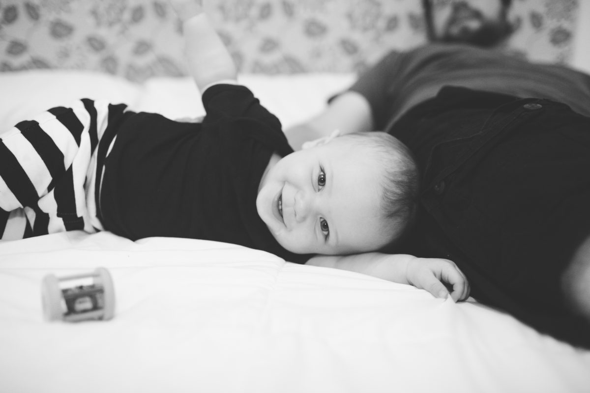 baby laying on side on bed laughing in black and white striped pants