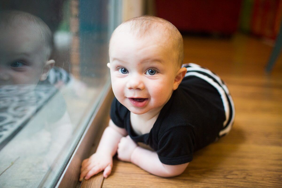 baby laying on floor smiling with reflection in window