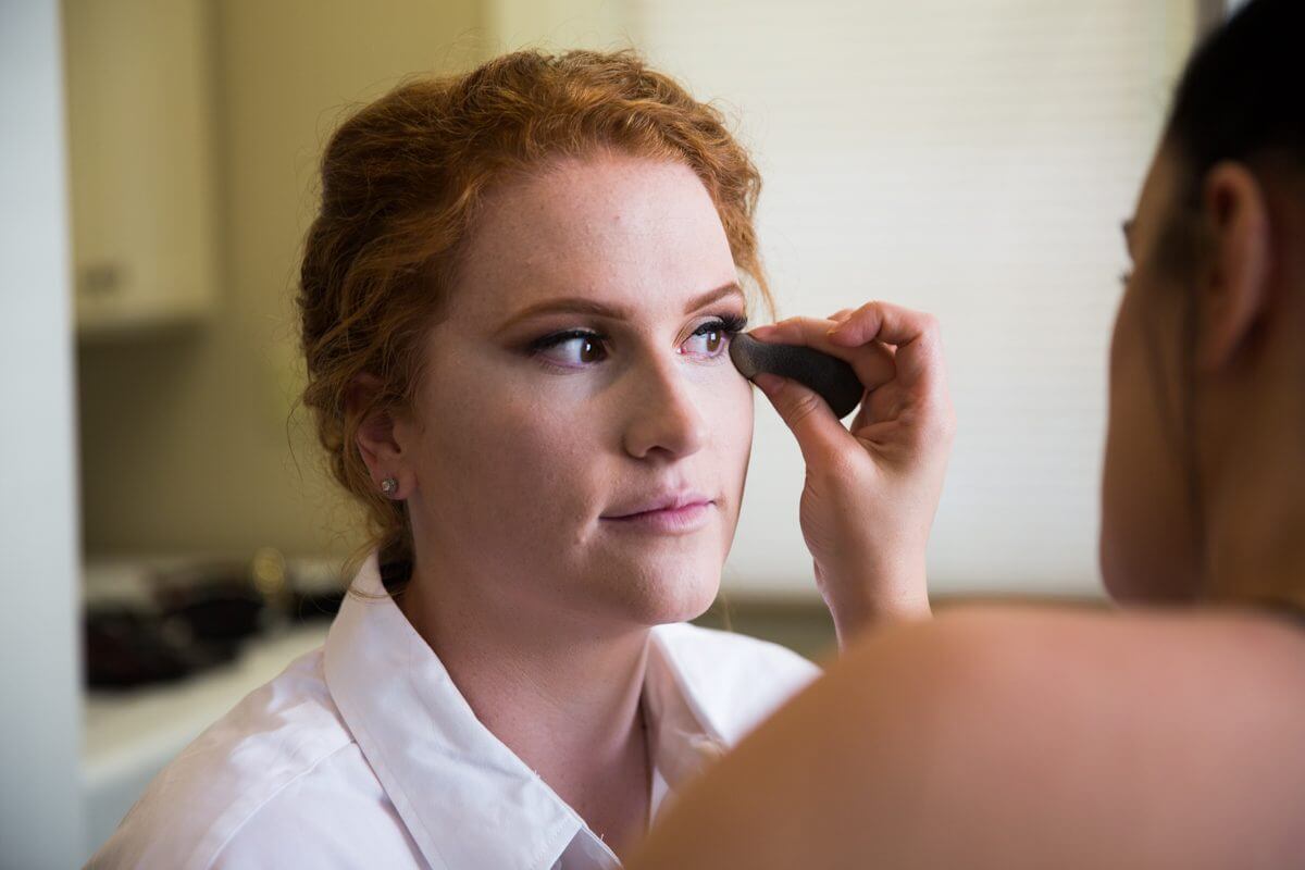 Redheaded bride in makeup session with aesthetician 