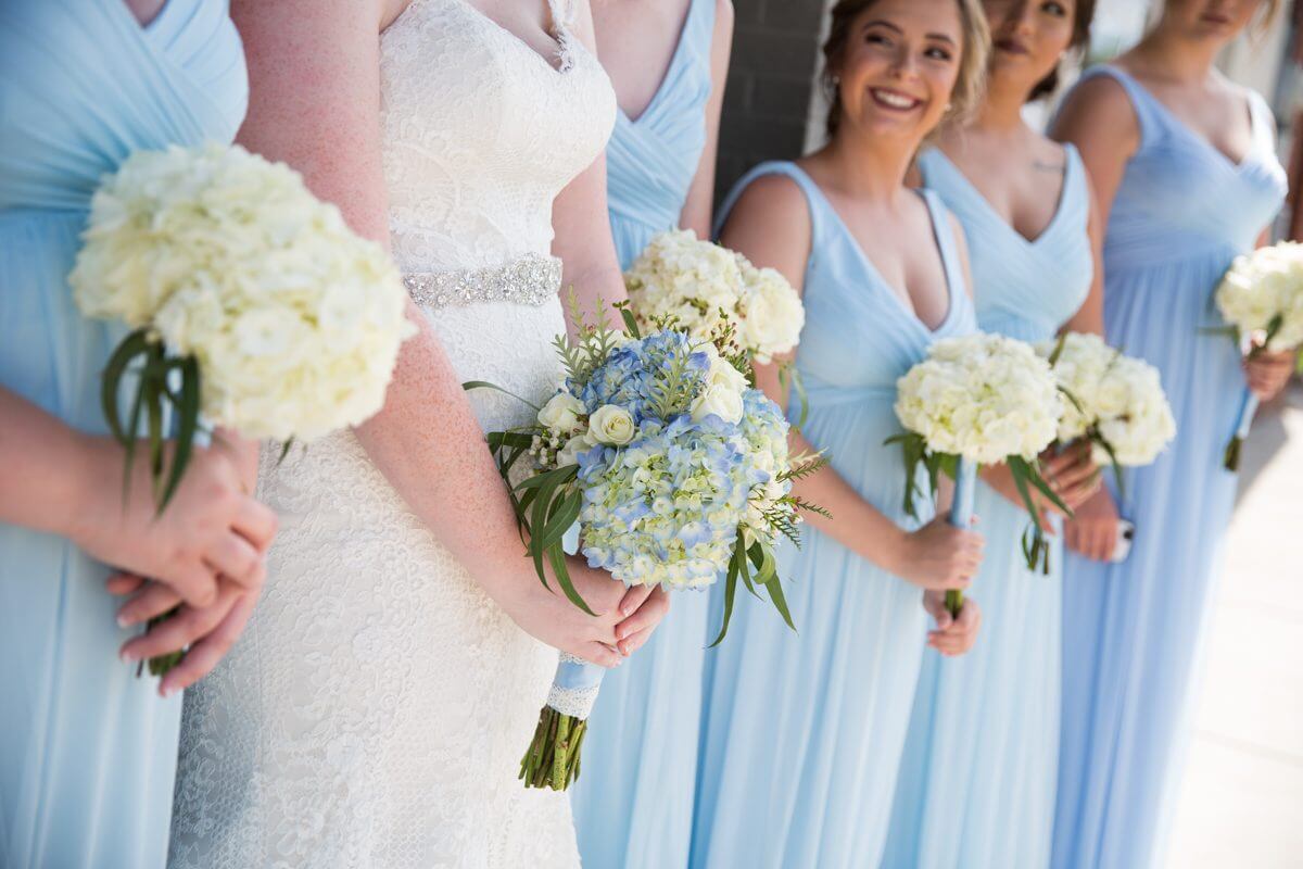 profile view of brides maids in blue dresses and bride in white dress holding flower bouquets