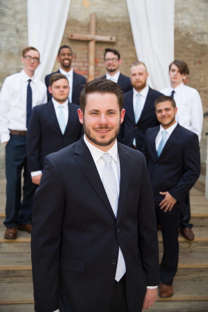 groom and groomsmen in front of cross on brick wall at the Norton Building in Ruston, LA