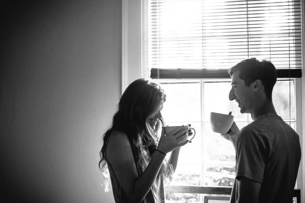 couple drinking coffee in front of kitchen window during an at home engagement session in Shreveport, Louisiana
