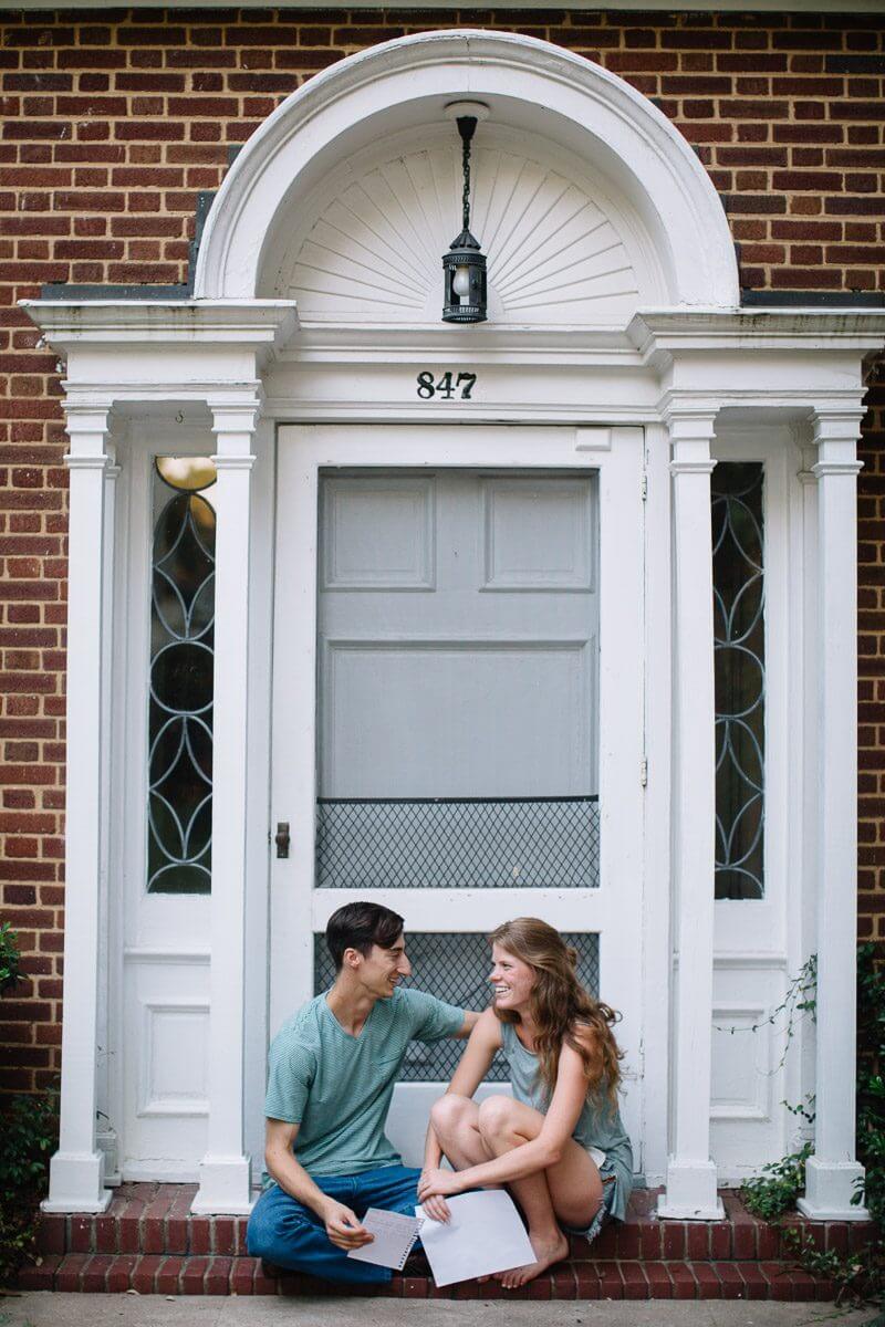 couple sitting on the stoop outside their white wooden front door and stoop and holding love letters they have written one another