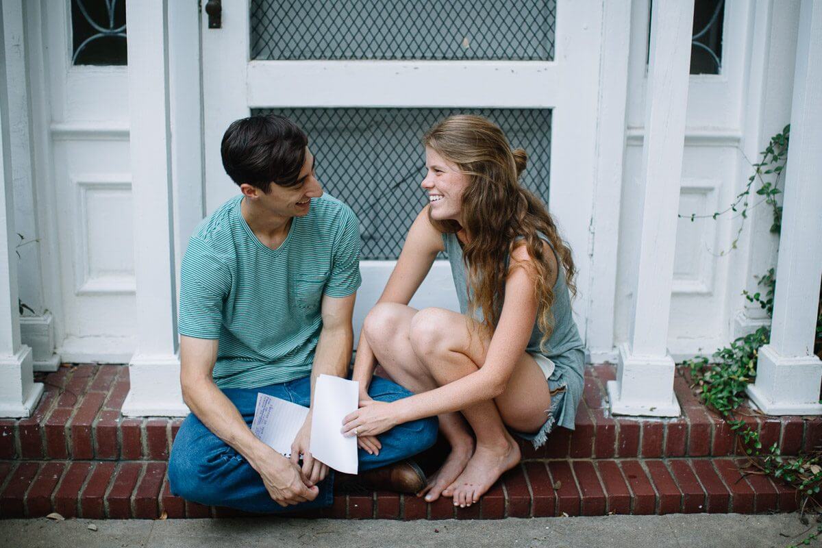 couple sitting on their front stoop smiling at one another and holding love letters they have written