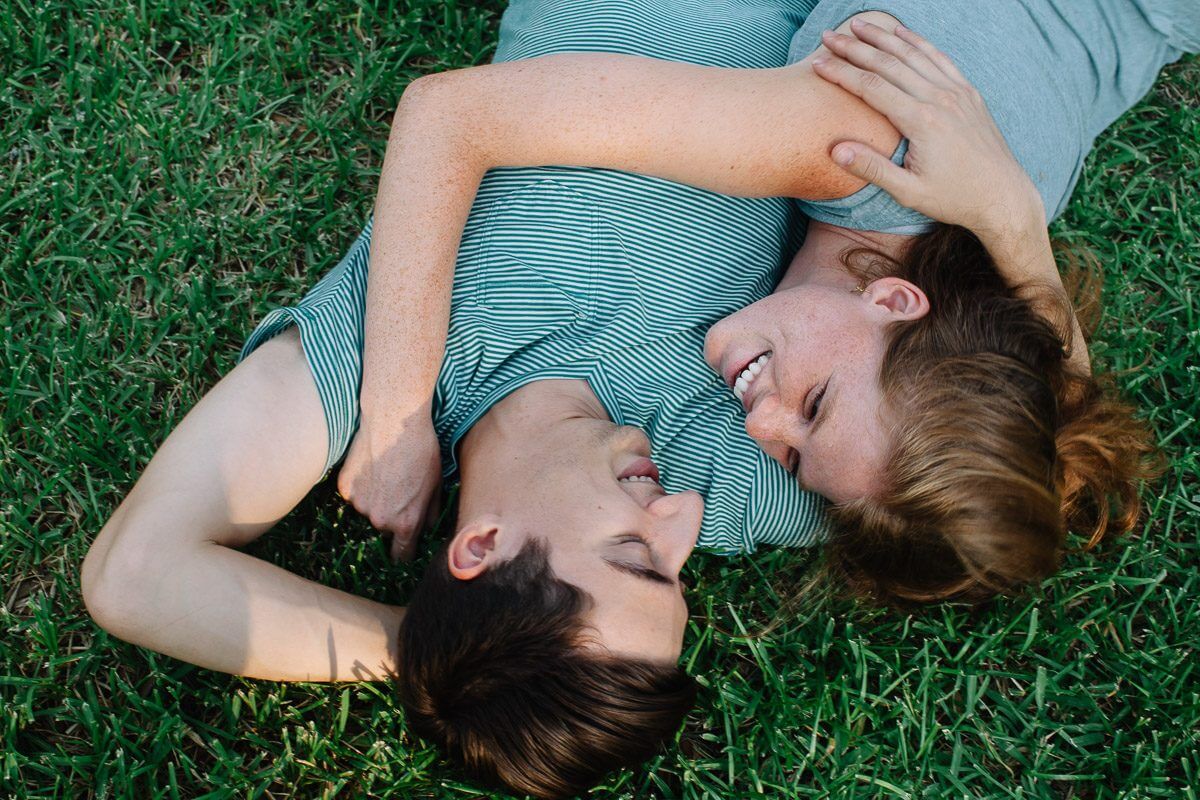couple holding each other while laying in the grass and smiling at one another