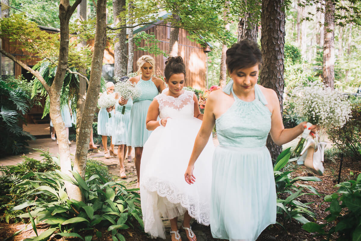 bride and bridesmaids exiting dressing room in a line and walking amidst ferns and trees